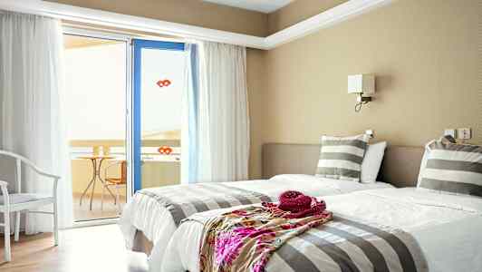 Et hotelværelse med to enkeltsenge, stribet sengetøj og en dør til en altan. (AI-genereret tekst)