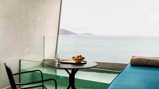 En terrasse med bord, stol og et siddeområde ved en lille pool med udsigt over havet. (AI-genereret tekst)