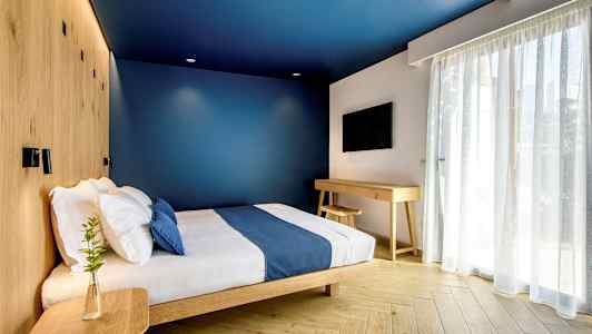 Et moderne hotelværelse med blå vægge, en seng med blå sengetæppe og træmøbler. (AI-genereret tekst)