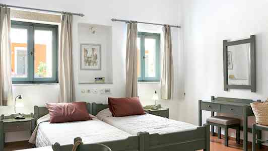 Billede af et lyst soveværelse med to enkeltsenge, vinduer med lysindfald og træmøbler. (AI-genereret tekst)