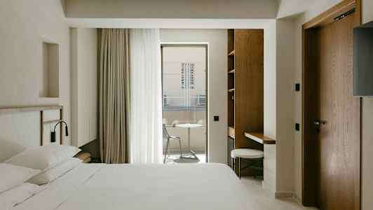 Et hotelværelse med en dobbeltseng, skrivebord og altan med havemøbler. (AI-genereret tekst)