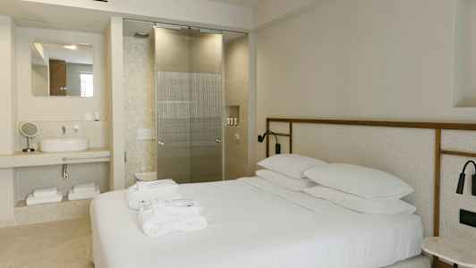 Moderne indrettet hotelværelse med en dobbeltseng, håndvask og glasdør til badeværelset. (AI-genereret tekst)