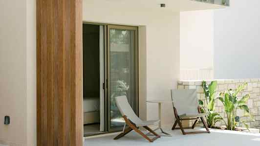 En terrasse med to stole, et lille bord og grønne planter ved en glasdør. (AI-genereret tekst)