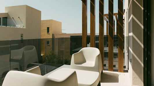 To hvide stole og et bord på en altan med glasrækværk og træpaneler. (AI-genereret tekst)