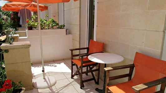 Udendørsterrasse med to orange stole og et hvidt bord under en parasol. (AI-genereret tekst)