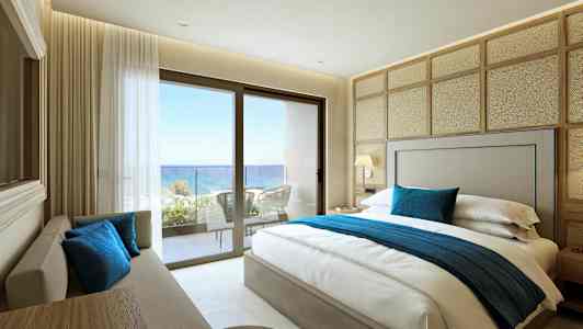 Et hotelværelse med en dobbeltseng, sofa og udsigt over havet fra en balkon. (AI-genereret tekst)