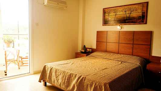 Et soveværelse med en seng, et natbord og et maleri på væggen; ved siden af er en åben altandør. (AI-genereret tekst)