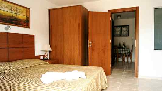 Billede af et hotelværelse med en seng, et natbord, et skab og en dør der fører til spiseområdet. (AI-genereret tekst)