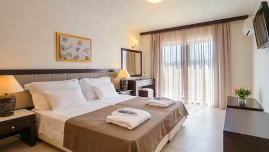 Hotelværelse med dobbeltseng, natbord og store vinduer med lyse gardiner. (AI-genereret tekst)