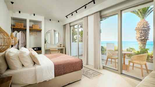 Moderne hotelværelse med seng, skrivebord, garderobe og altan med havudsigt. (AI-genereret tekst)