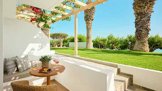 Udendørs spiseområde med bord og stole i en have med palmer og havudsigt. (AI-genereret tekst)