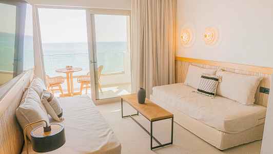 Et hotelværelse med siddepladser og balkon med udsigt til havet. (AI-genereret tekst)