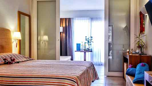 Et hotelværelse med en seng med et stribet sengetæppe. Værelset har også et bord med dekorative genstande og baggrund med glasvægge. (AI-genereret tekst)