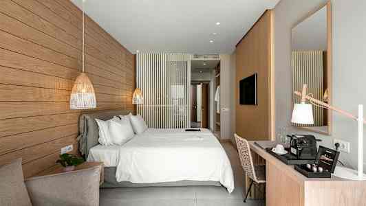 Et lyst og moderne hotelværelse med en stor dobbeltseng, et skrivebord og en dekorativ marmorpanel på væggen. (AI-genereret tekst)