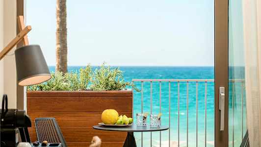 Udsigt fra en balkon mod havet med et bord, der har frugt og drikke på sig. (AI-genereret tekst)