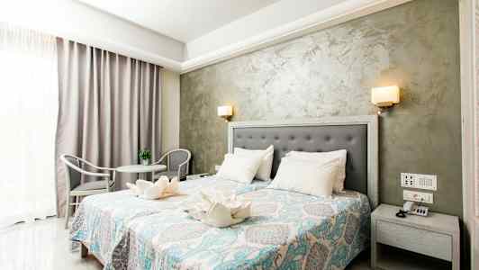 Et hotelværelse med dobbeltseng, natbord, dekorativt sengetæppe og siddegruppe. (AI-genereret tekst)