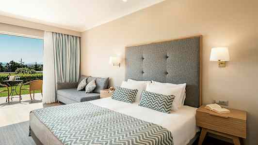 Hotelværelse med dobbeltseng og siddeområde samt adgang til terrasse med naturlig udsigt. (AI-genereret tekst)