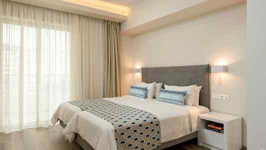 Dobbeltværelse med en grå sengegavl, hvide sengelagner og blåmønstrede puder og sengetæppe, oplyst af væglamper. (AI-genereret tekst)