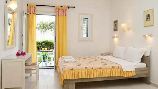 Hotelværelse med en opredt seng og åbne glasdøre mod en terrasse med stole og et bord (AI-genereret tekst)