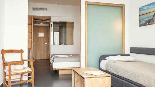 Et hotelværelse med to senge, en stol og et bord. (AI-genereret tekst)