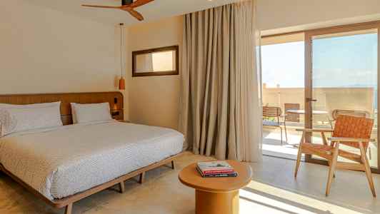 Værelse med dobbeltseng, bord og stol, samt glasdør til terrasse. (AI-genereret tekst)