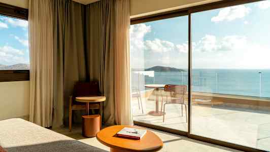 Moderne hotelværelse med store glasdøre, der fører ud til en altan med havudsigt. (AI-genereret tekst)