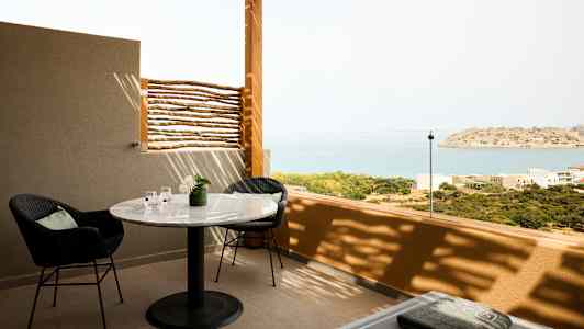 En terrasse med et bord, stole og udsigt over havet og en lille ø. (AI-genereret tekst)