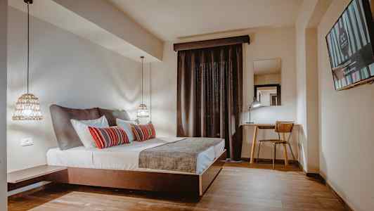 Et hotelværelse med en dobbeltseng, skrivebord og stol samt et TV på væggen. (AI-genereret tekst)