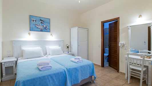 Et hotelværelse med to enkeltsenge med blå sengelinned og hvide puder, et skab, et skrivebord med spejl og et badeværelse med åben dør. (AI-genereret tekst)