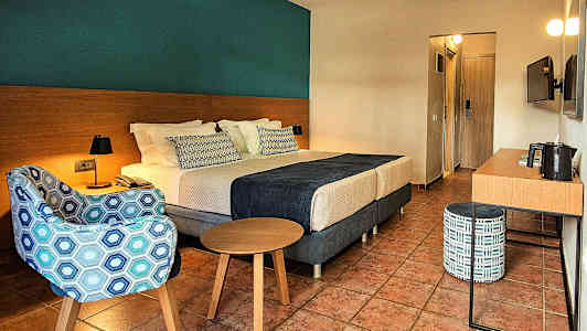 Et hotelværelse med en dobbeltseng, lænestol, bord og skrivebord. (AI-genereret tekst)