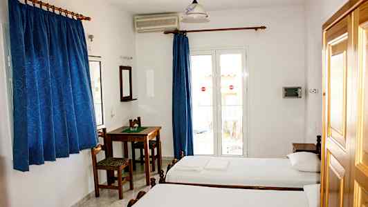 Et hotelværelse med to enkeltsenge, et bord med stole, blå gardiner og en altandør. (AI-genereret tekst)