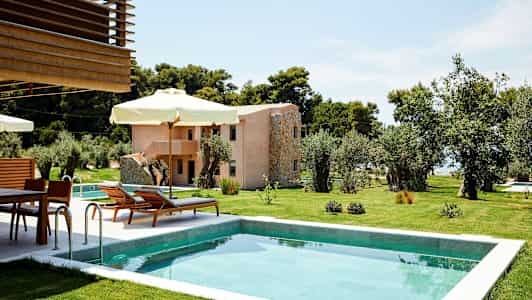 En pool omgivet af grønne græsplæner og solsenge med parasoller, med en bygning i baggrunden. (AI-genereret tekst)