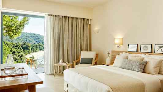 Et hotelværelse med en dobbeltseng, siddeområder og et stort vindue med udsigt over et frodigt landskab. (AI-genereret tekst)