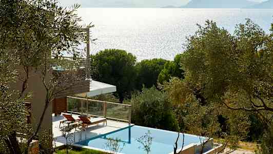 En villa med privat pool omgivet af træer med udsigt over havet og bjerge i baggrunden. (AI-genereret tekst)