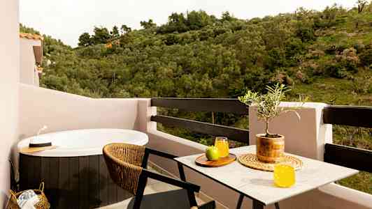 En balkon med et spabad, et bord med saftglas og frugt samt udsigt over grønne områder. (AI-genereret tekst)