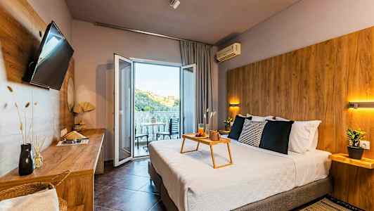 Moderne hotelværelse med dobbeltseng, siddeplads på altanen og udsigt over et grønt bakket landskab. (AI-genereret tekst)