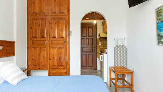 Et værelse med en seng, trærskabe, strygebræt og en åbning til et køkken. (AI-genereret tekst)