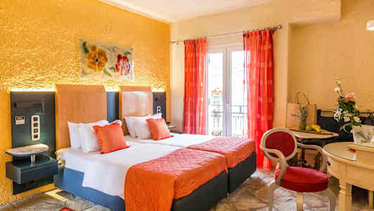 Et hotelværelse med to senge, orange indretning og røde gardiner samt et mindre bord med stole og dekorationer. (AI-genereret tekst)