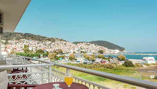 Udsigt over en by med hvide huse og røde tage, ved havet, fra en altan med bord og drikke. (AI-genereret tekst)