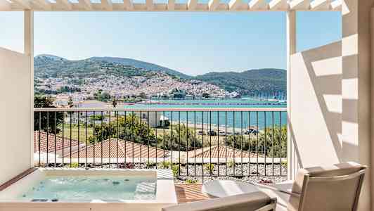 Udsigt fra en terrasse med to stole og et spabad, mod en kystby med bjerge i baggrunden. (AI-genereret tekst)