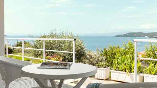 Udsigt over havet fra en terrasse med et bord og stole. (AI-genereret tekst)