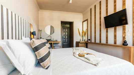 Et moderne hotelværelse med en redt seng, dekorative træpaneler og et tv på væggen. (AI-genereret tekst)