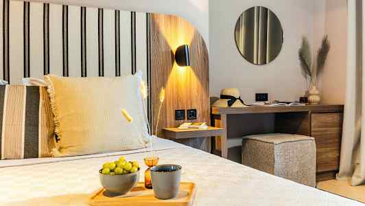 Et moderne hotelværelse med trædekoration, en seng med dekorative puder, et skrivebord med spejl og dekorative genstande, og grønne druer på en tallerken. (AI-genereret tekst)