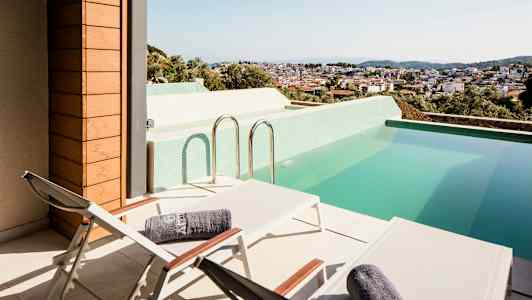 Terrasse med liggestole og en pool med udsigt over en by. (AI-genereret tekst)