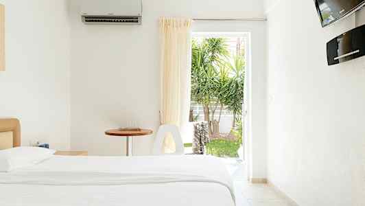 Et lyst hotelværelse med en seng, et bord og en åbning mod en have. (AI-genereret tekst)