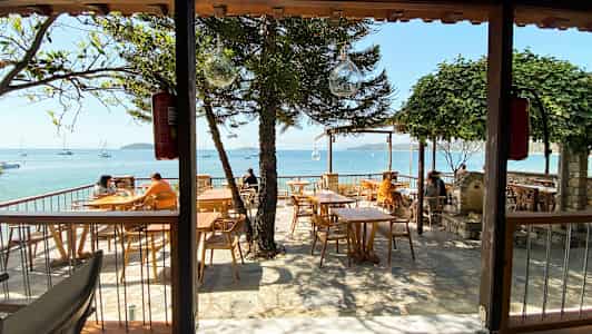 Udendørs restaurant med havudsigt og træborde. (AI-genereret tekst)