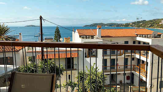 Udsigt over huse med røde tage, palmetræer og hav i baggrunden. (AI-genereret tekst)