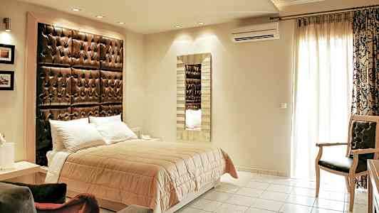 Et soveværelse med en dobbeltseng, en stor polstret sengegavl og et spejl på væggen. (AI-genereret tekst)