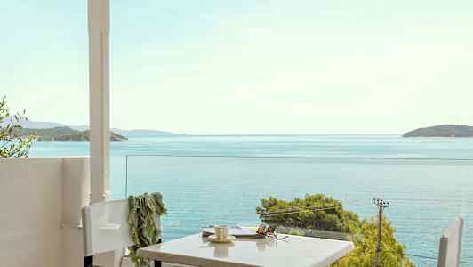 Udsigt mod havet fra en terrasse med bord og stole. (AI-genereret tekst)