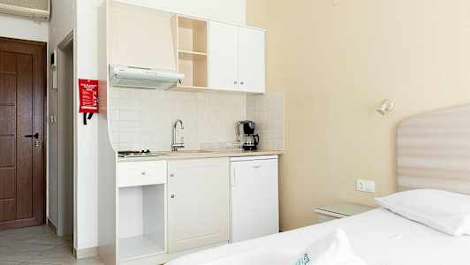 Lille tekøkken med hvide køkkenmøbler i et værelse med en seng. (AI-genereret tekst)